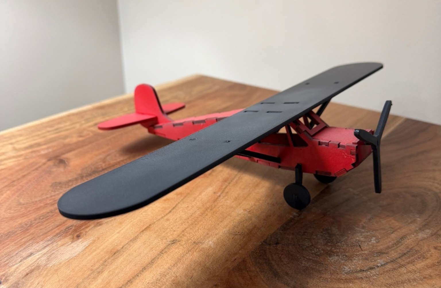 Red and black wooden model airplane with black wing, propeller and landing gear