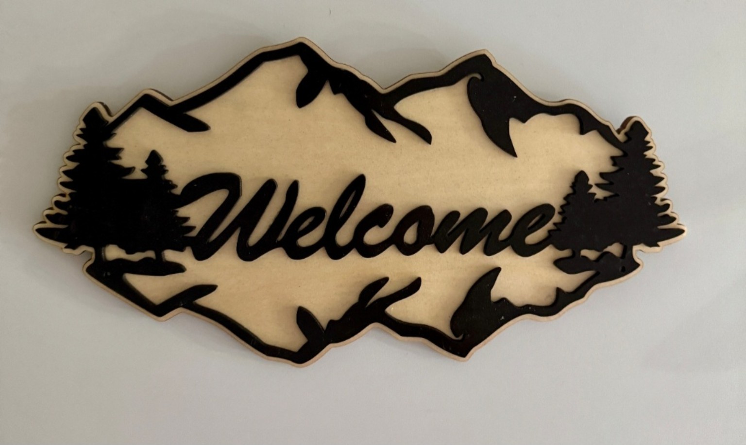 Light wooden Welcome sign with black mountain and evergreen silhouettes and bold lettering