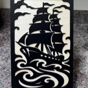 Eight by eleven inch black and natural wood sailing ship artwork with sails, curling waves and a small display stand
