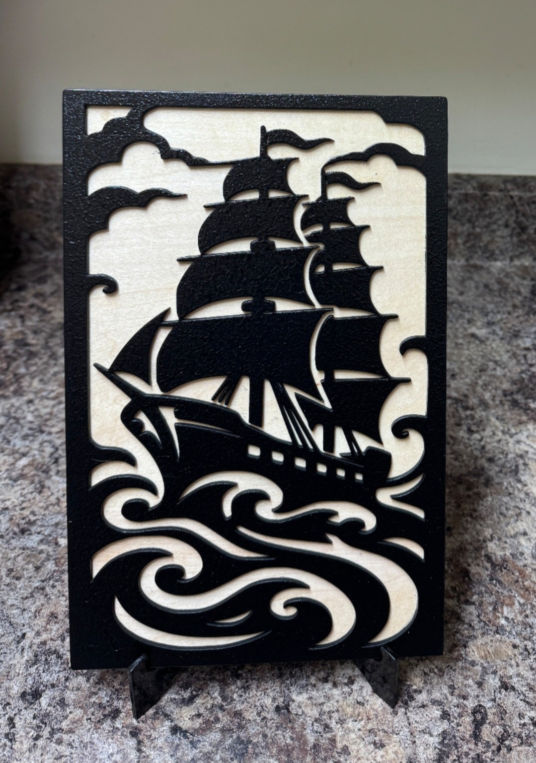 Eight by eleven inch black and natural wood sailing ship artwork with sails, curling waves and a small display stand