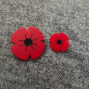 Small red acrylic Remembrance Day poppy with a black centre, shown beside a larger matching poppy